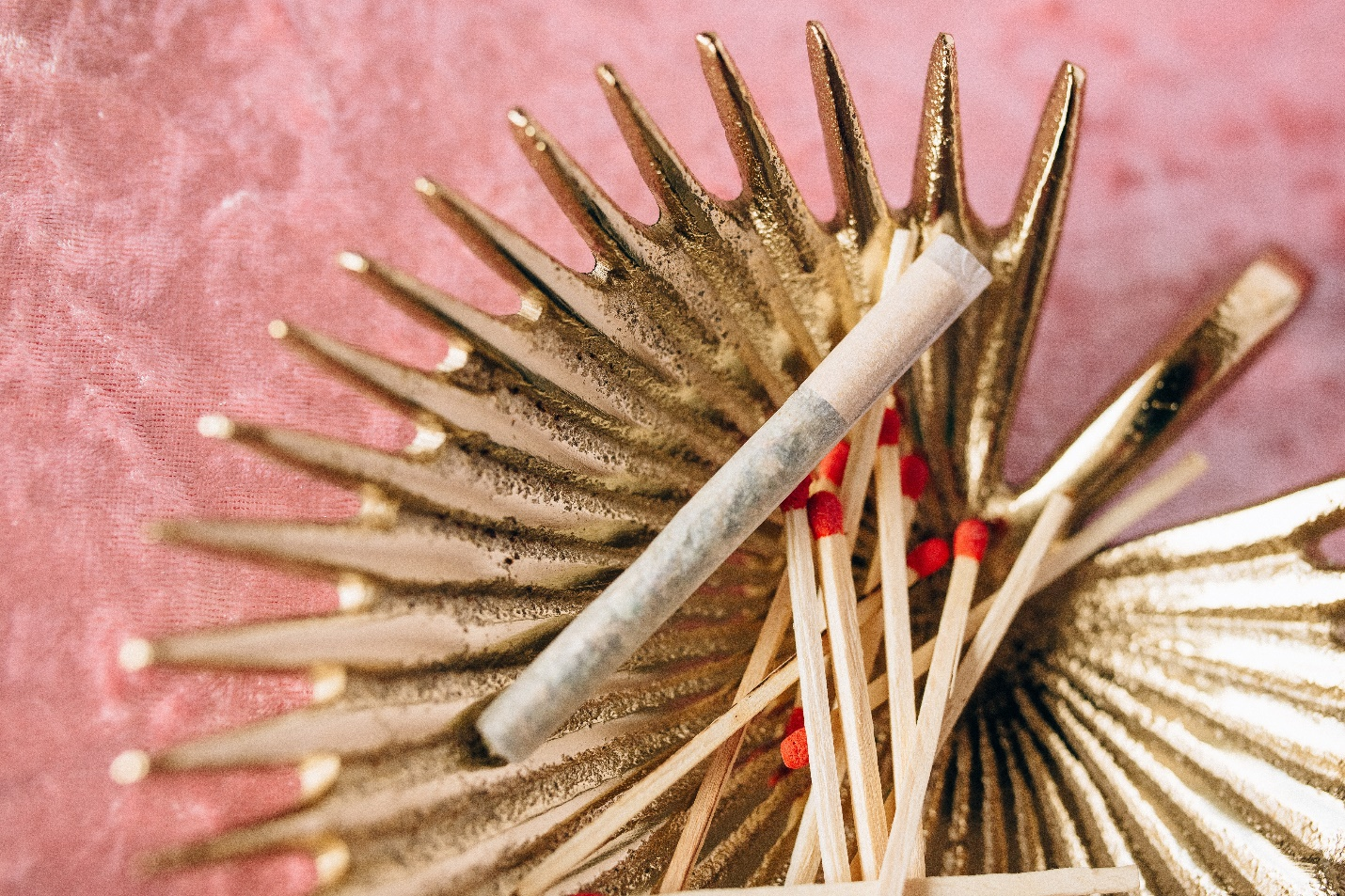 A joint and matches sit in a golden tray on a pink velvet textile