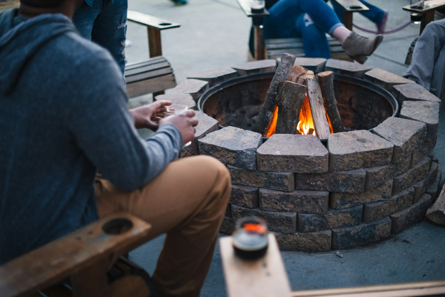 People sit around an outdoor bonfire surrounded by bricks