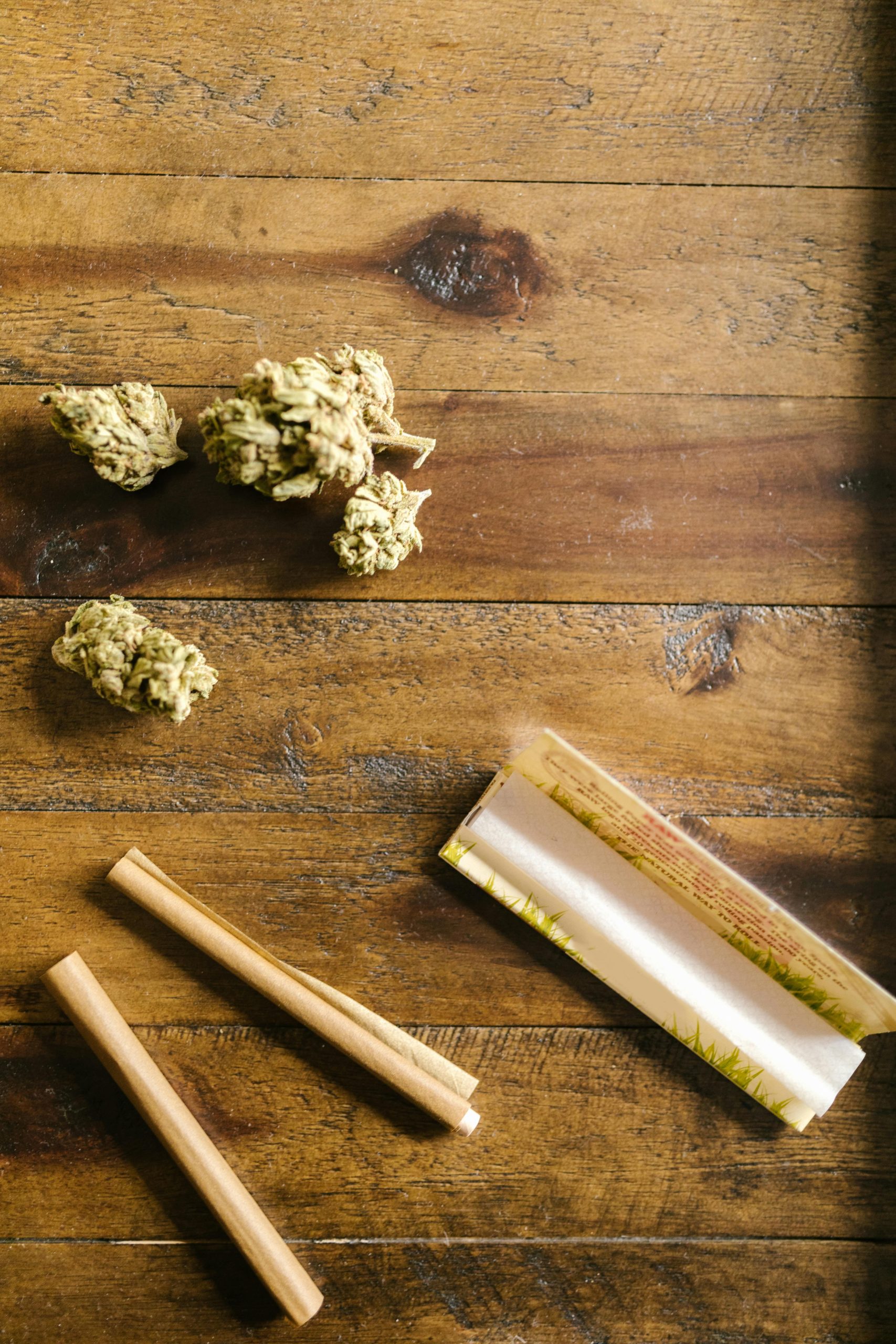 Pre-roll paper and loose cannabis flower arranged on wood