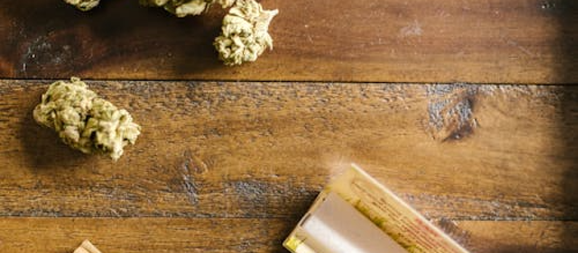 Cannabis flower with rolling paper on a wooden surface, symbolizing personalized cannabis use and premium pre-roll selection